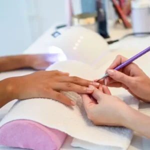 Manicure spa klasyczny, hybrydowy i japoński. Kosmetolog trzyma dłoń klientki, poprawia kształt paznokci.