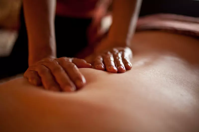 Dłonie terapeutki są ułożone na plecach klienta. Masażystka przygotowuje się do wykonania peelingu całego ciała.